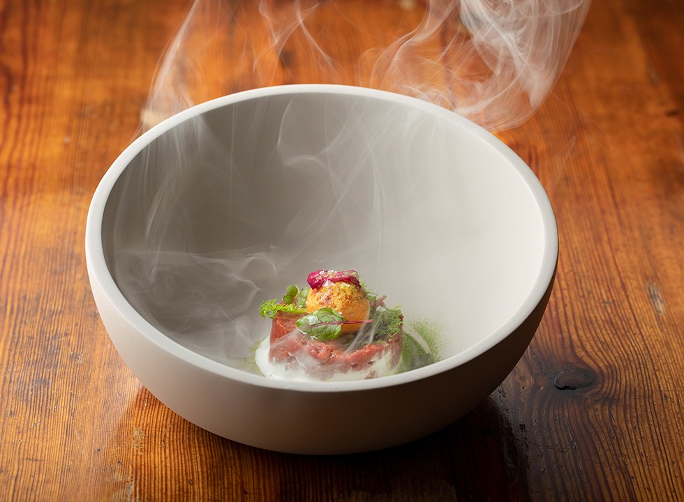 Ihr Vorgeschmack auf das Restaurant KITCHEN LIBRARY: Würziger Dry Aged Tatar mit Onsen-Ei, Rauch und marinierten Rosenblüten.